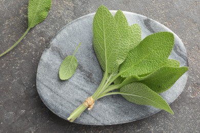 Photo of Bunch of green sage leaves on grey textured table, top view