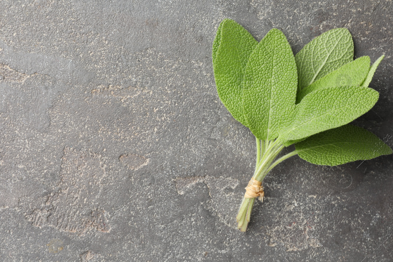 Photo of Bunch of green sage leaves on grey textured table, top view. Space for text