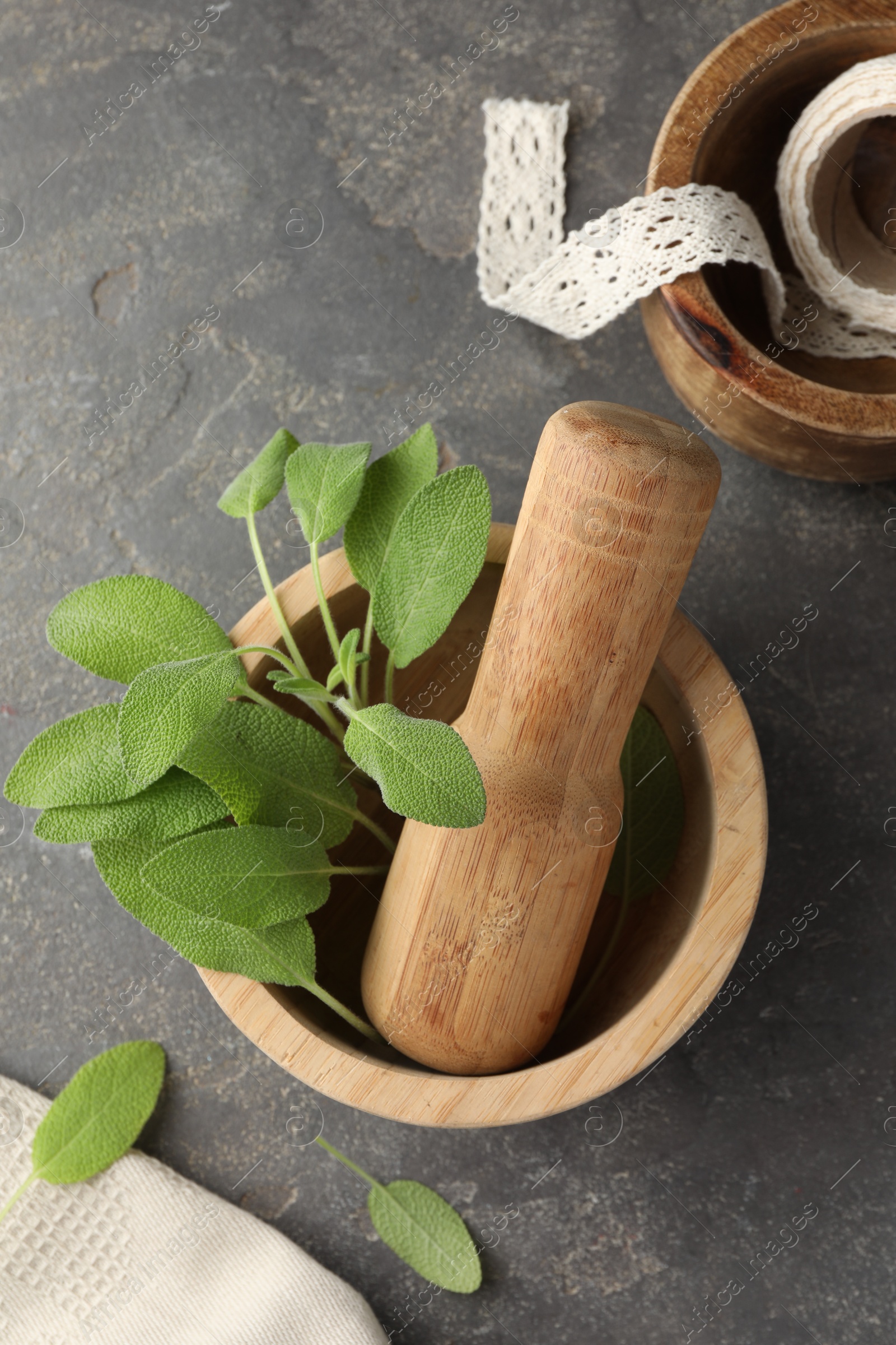 Photo of Green sage leaves in mortar with pestle on grey textured table, flat lay