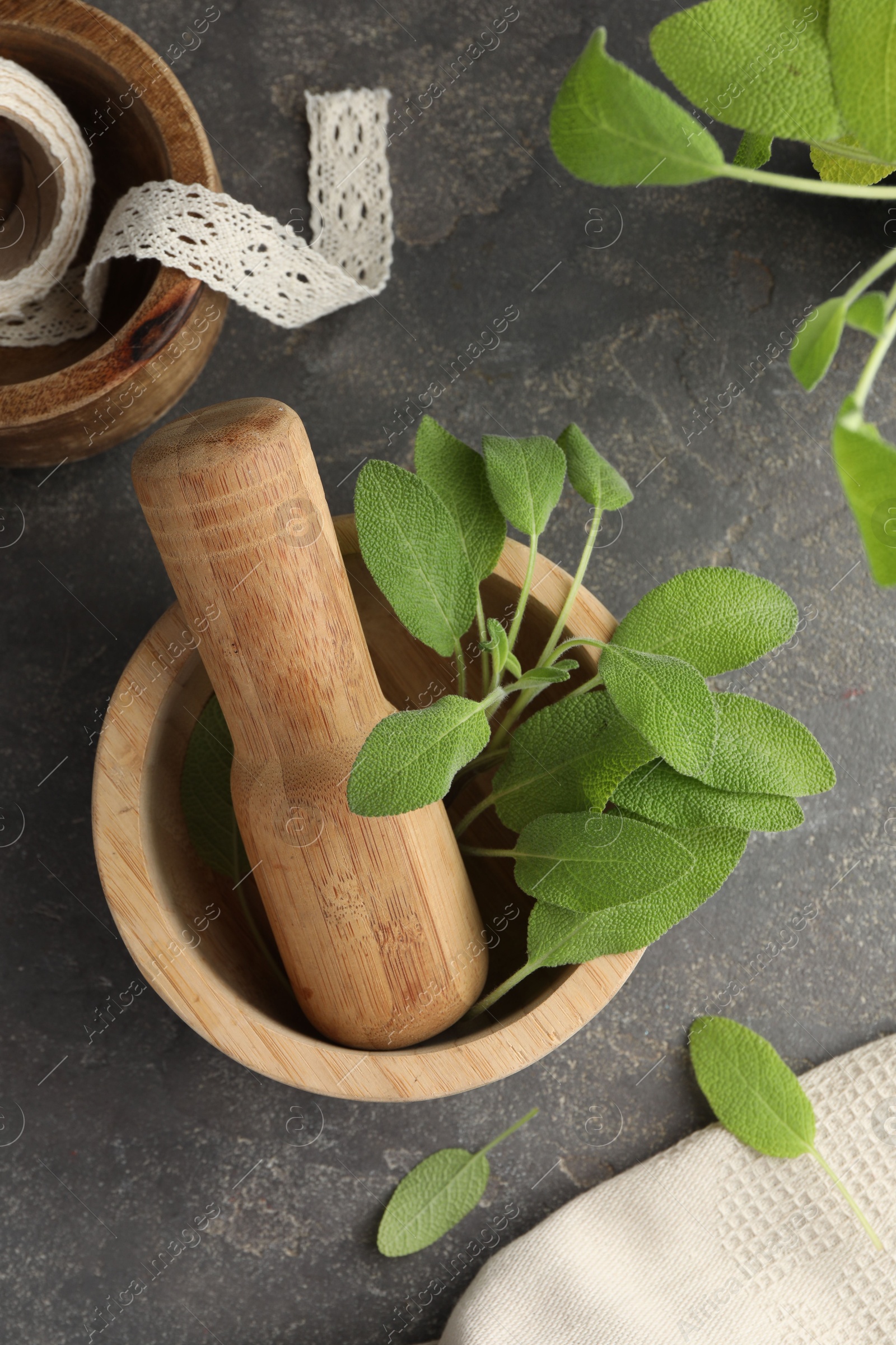 Photo of Green sage leaves in mortar with pestle on grey textured table, flat lay