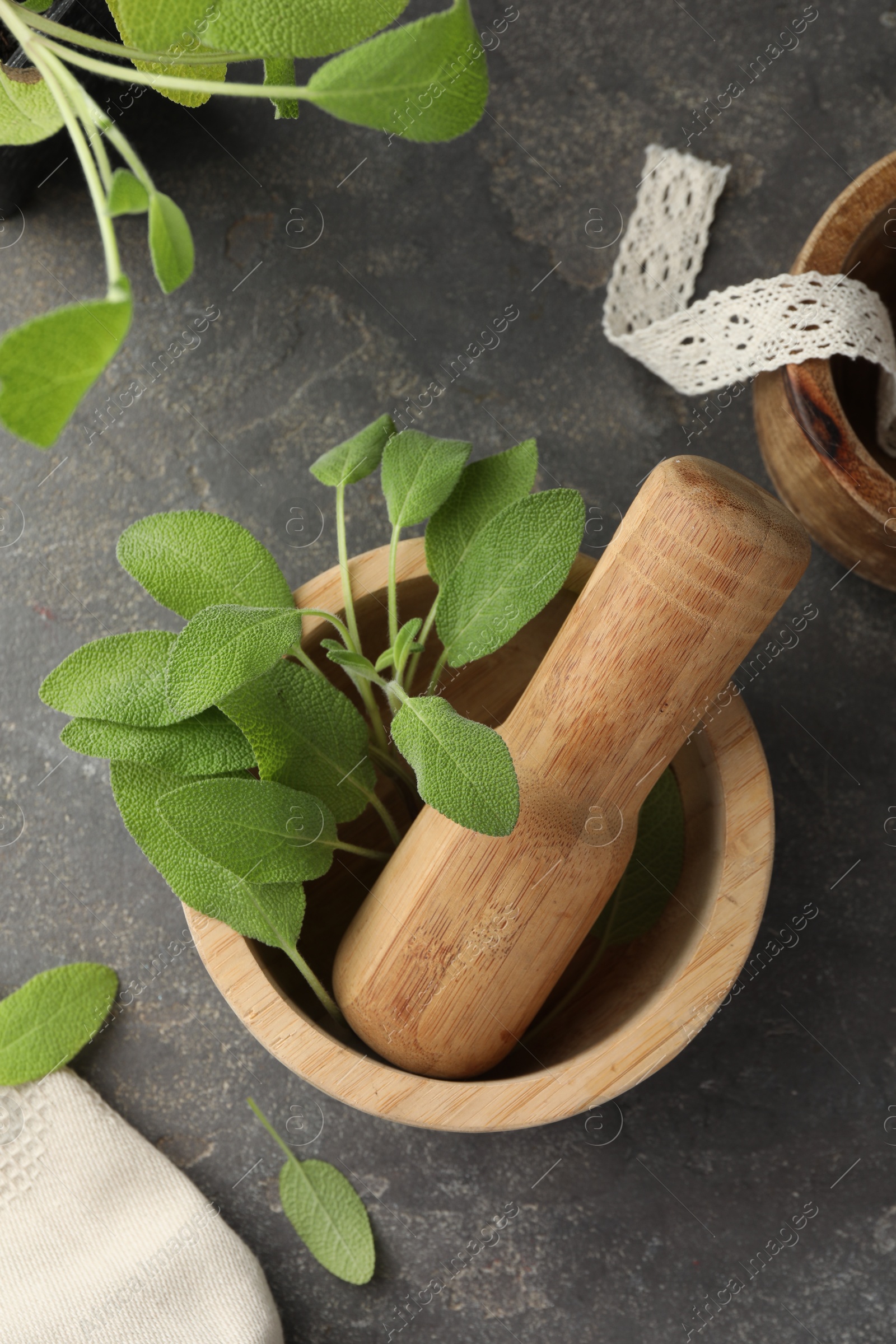 Photo of Green sage leaves in mortar with pestle on grey textured table, flat lay