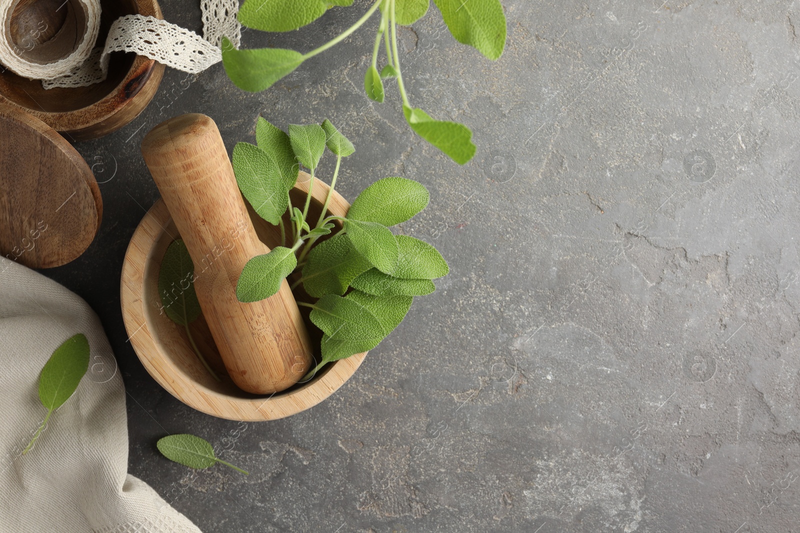 Photo of Green sage leaves in mortar with pestle on grey textured table, flat lay. Space for text