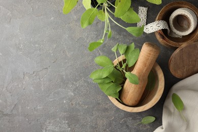 Photo of Green sage leaves in mortar with pestle on grey textured table, flat lay. Space for text