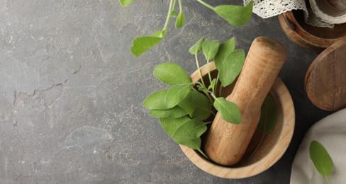 Photo of Green sage leaves in mortar with pestle on grey textured table, flat lay. Space for text