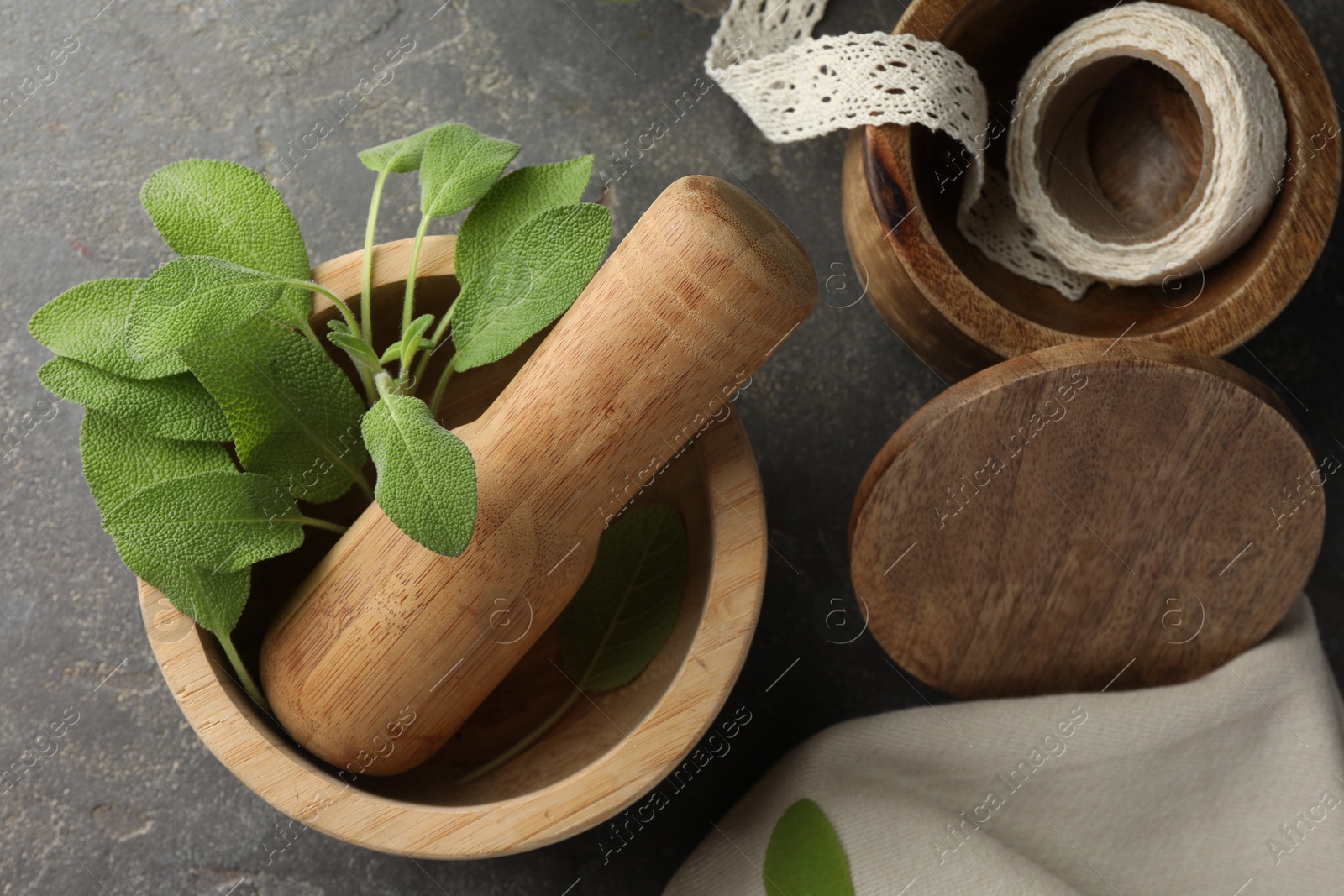 Photo of Green sage leaves in mortar with pestle on grey textured table, flat lay