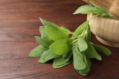 Photo of Green sage leaves on wooden table, closeup