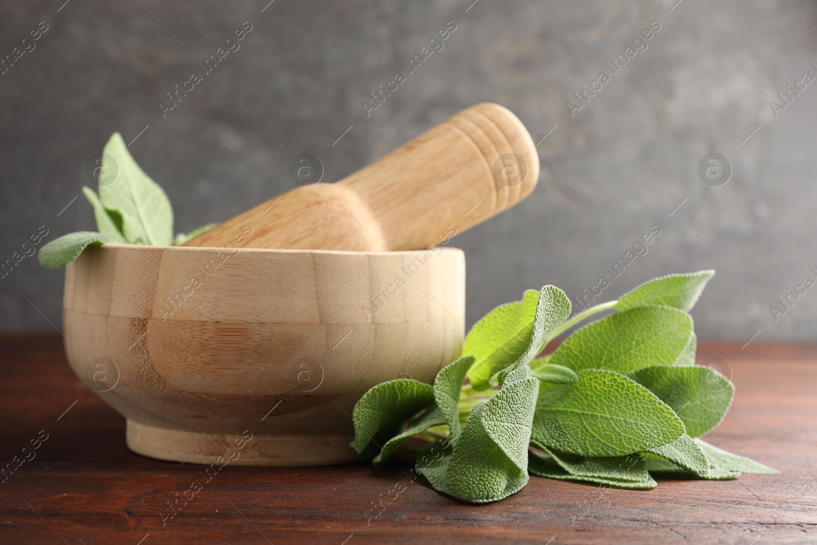 Photo of Green sage leaves, mortar and pestle on wooden table against grey background, closeup