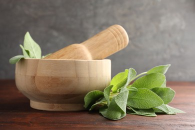 Photo of Green sage leaves, mortar and pestle on wooden table against grey background, closeup