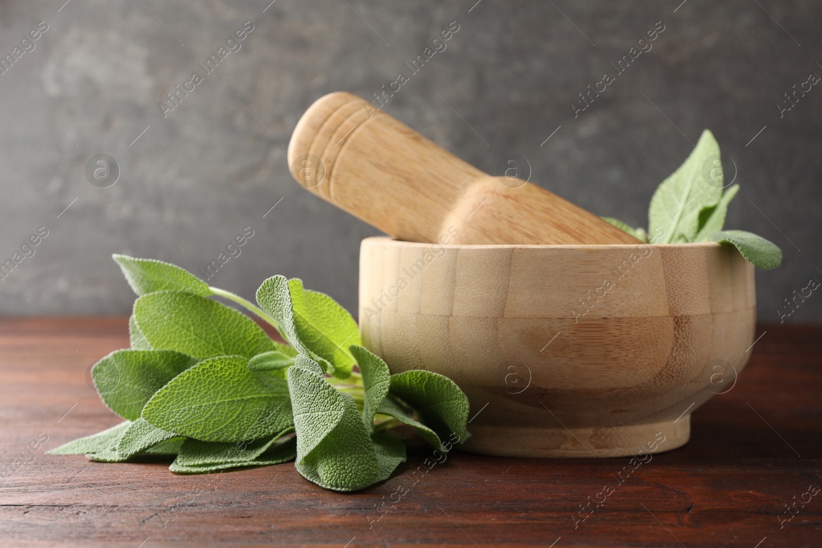 Photo of Green sage leaves, mortar and pestle on wooden table against grey background, closeup