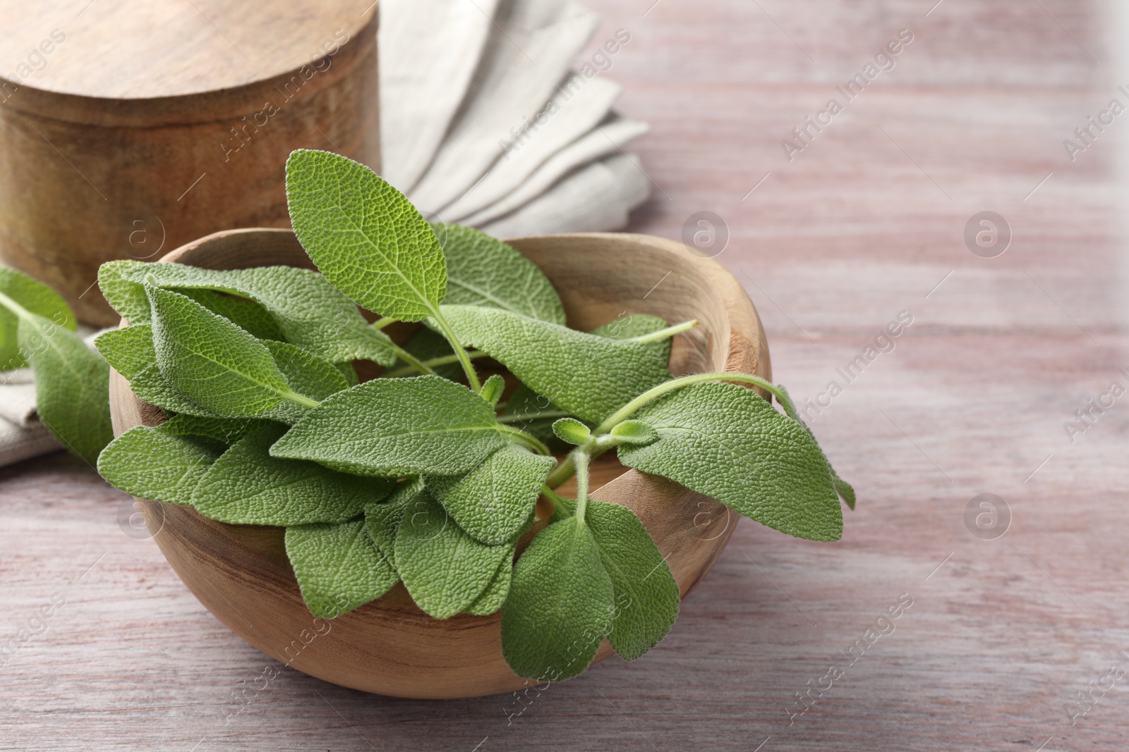 Photo of Green sage leaves in bowl on color wooden table, closeup