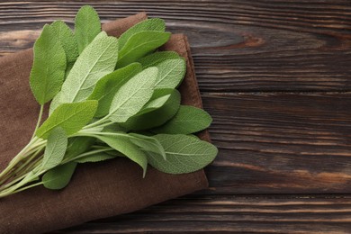 Photo of Napkin with green sage leaves on wooden table, top view. Space for text