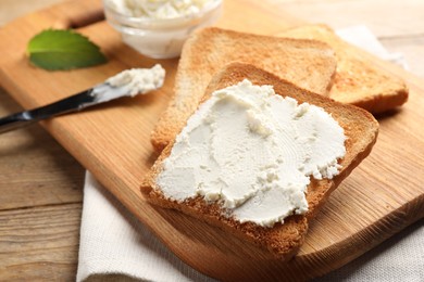 Photo of Delicious toasted bread slices with cream cheese on wooden table, closeup