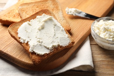 Delicious toasted bread slices with cream cheese on wooden table