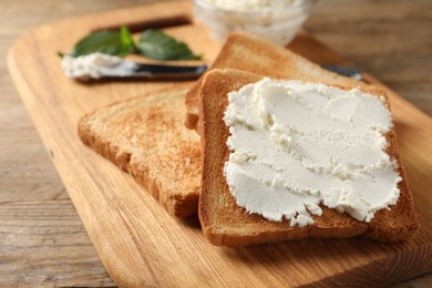 Delicious toasted bread slices with cream cheese on wooden table, closeup