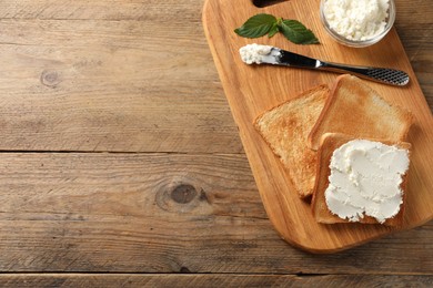 Delicious toasted bread slices with cream cheese, mint and knife on wooden table, top view. Space for text