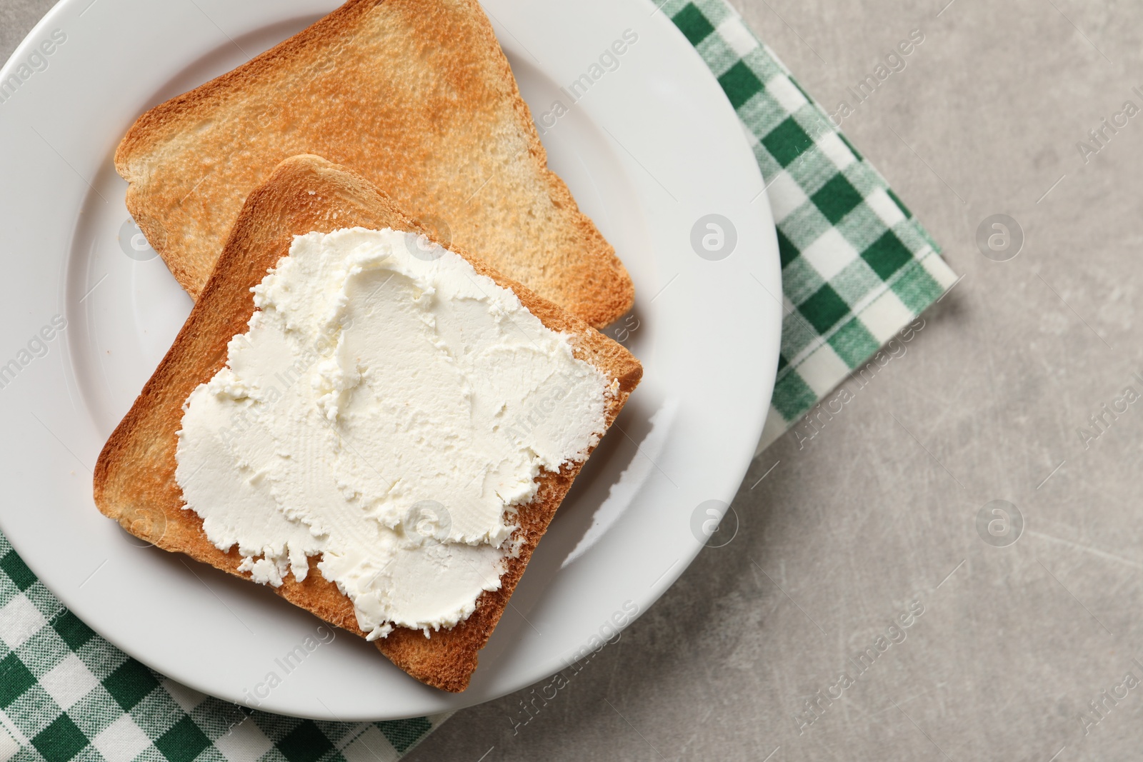 Photo of Delicious toasted bread slices with cream cheese on grey textured table, top view