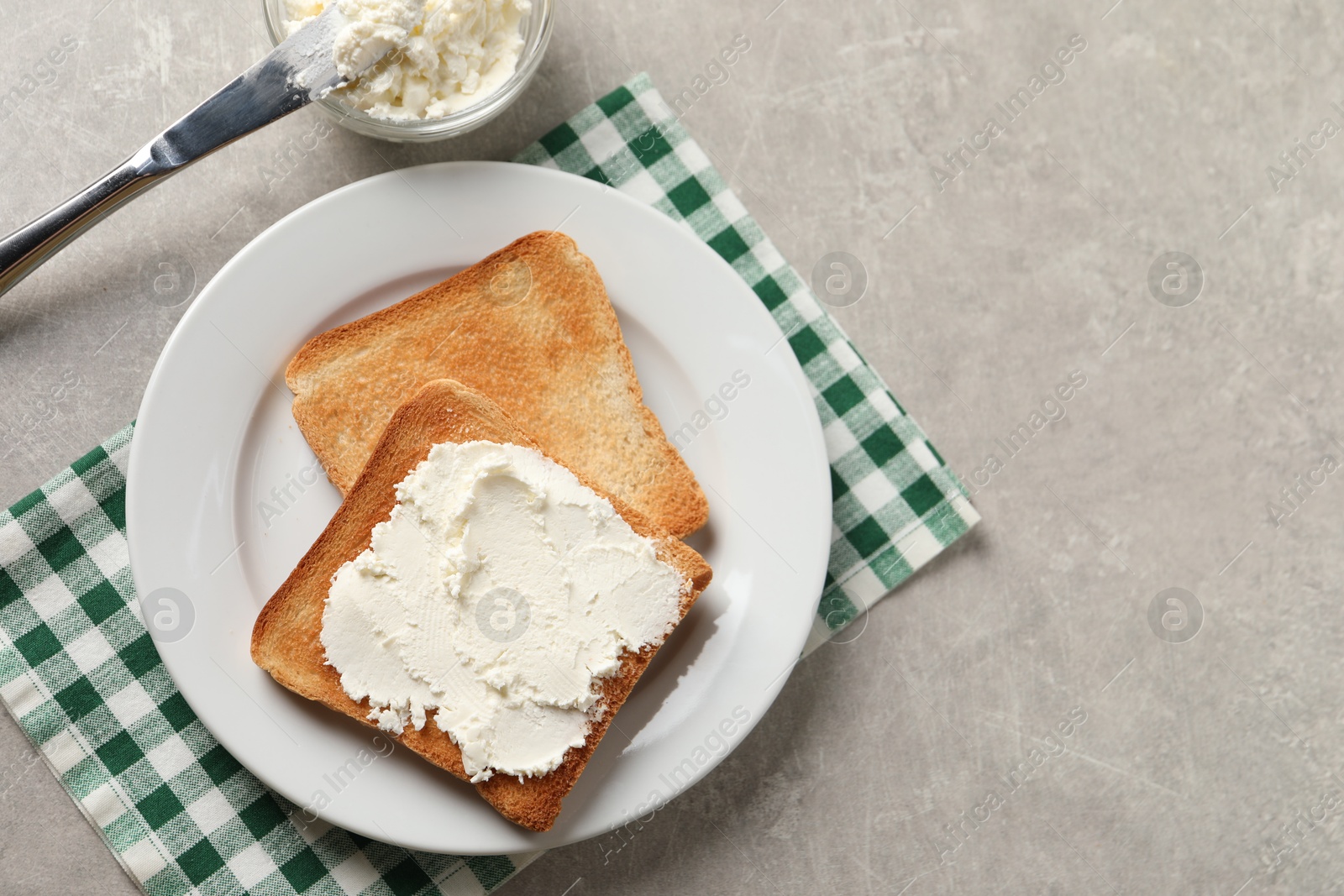 Photo of Delicious toasted bread slices with cream cheese and knife on grey textured table, flat lay. Space for text