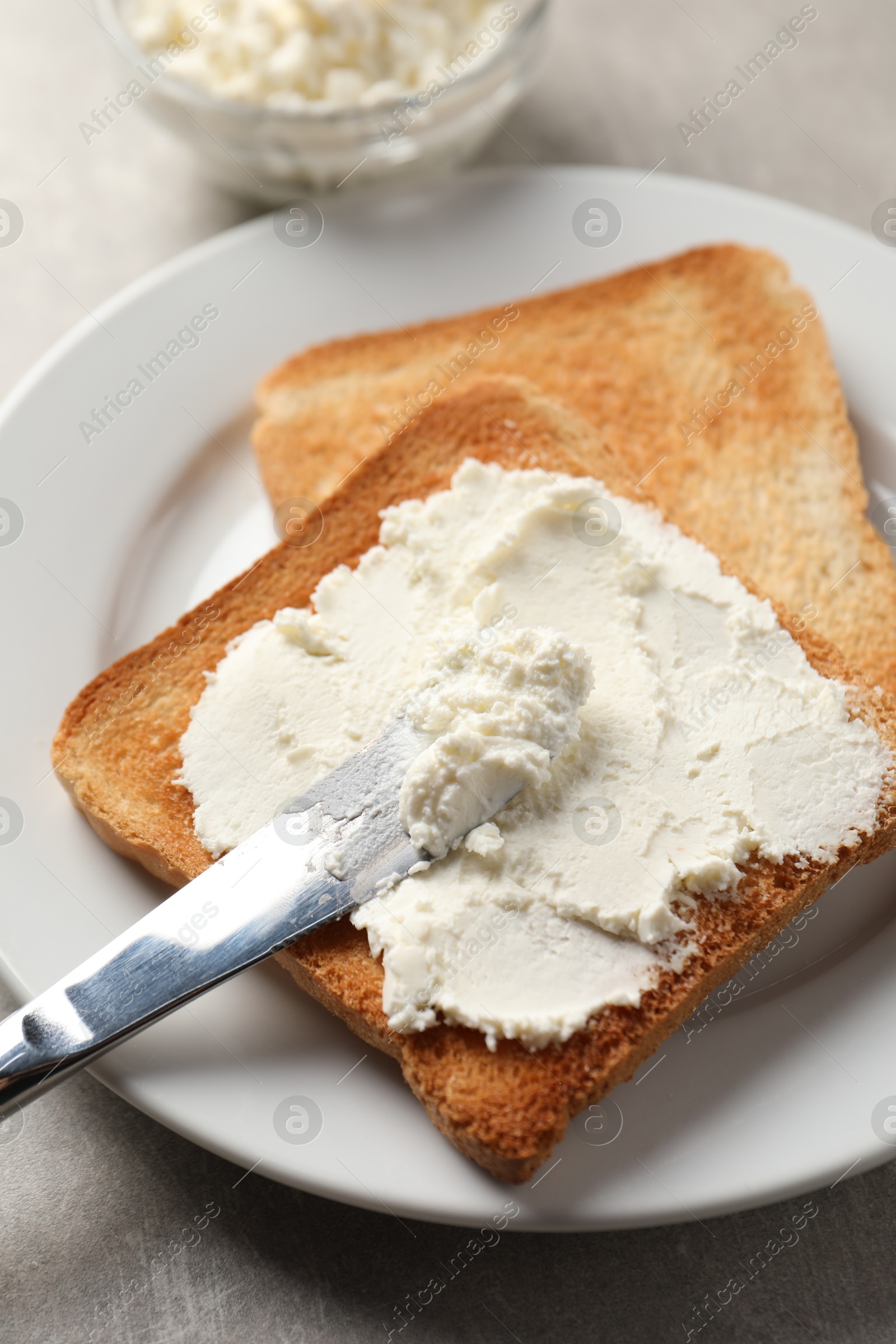 Photo of Delicious toasted bread slices with cream cheese and knife on grey table