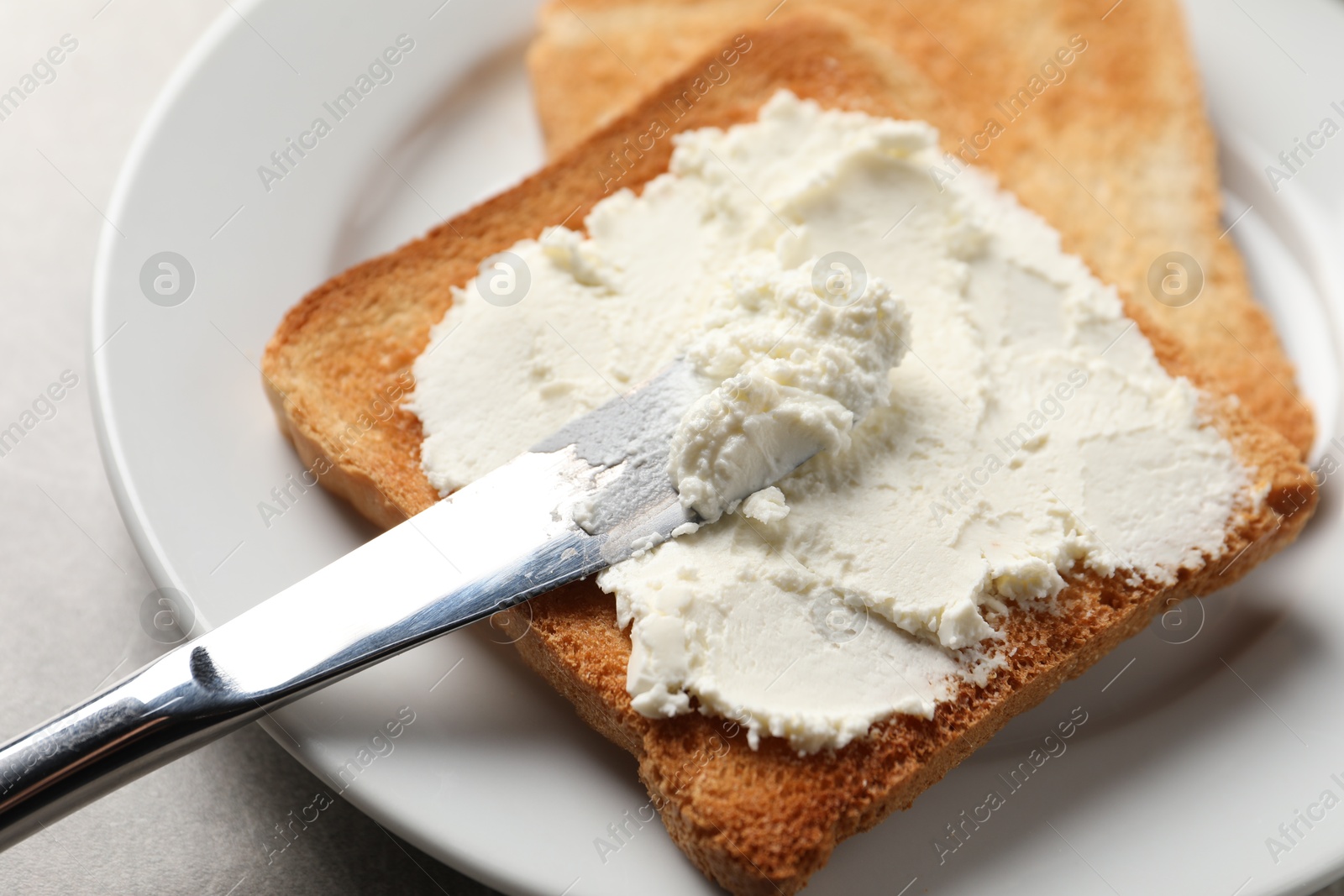 Photo of Delicious toasted bread slices with cream cheese and knife on grey table, closeup