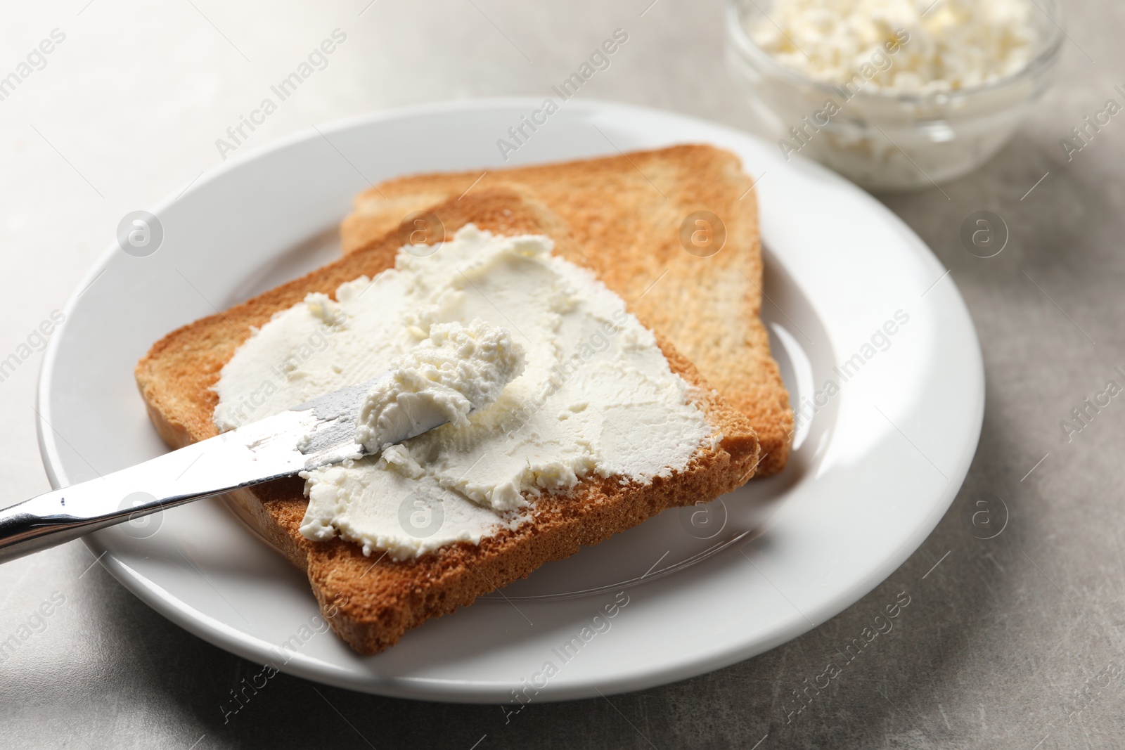 Photo of Delicious toasted bread slices with cream cheese and knife on grey table