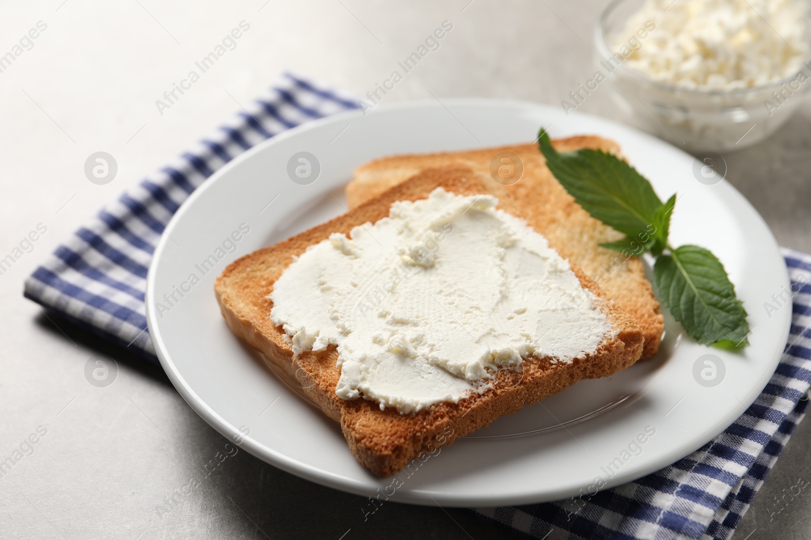 Photo of Delicious toasted bread slices with cream cheese and mint on grey table