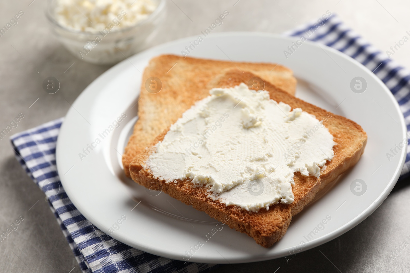 Photo of Delicious toasted bread slices with cream cheese on grey table