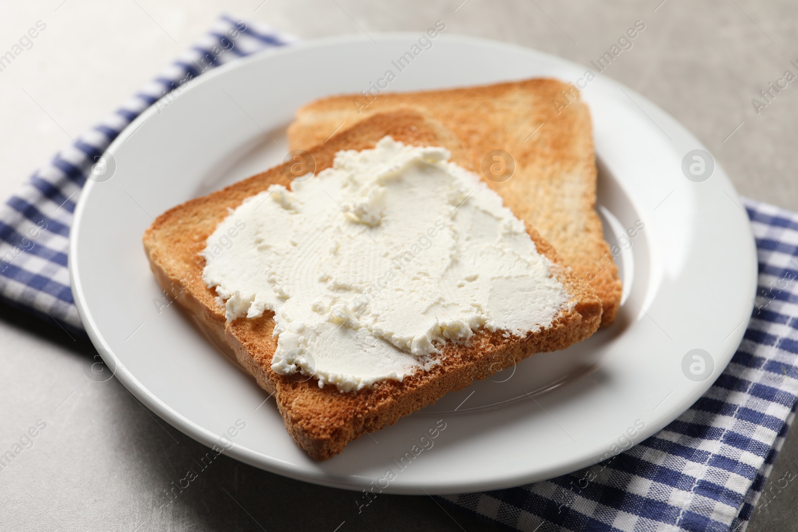 Photo of Delicious toasted bread slices with cream cheese on grey table