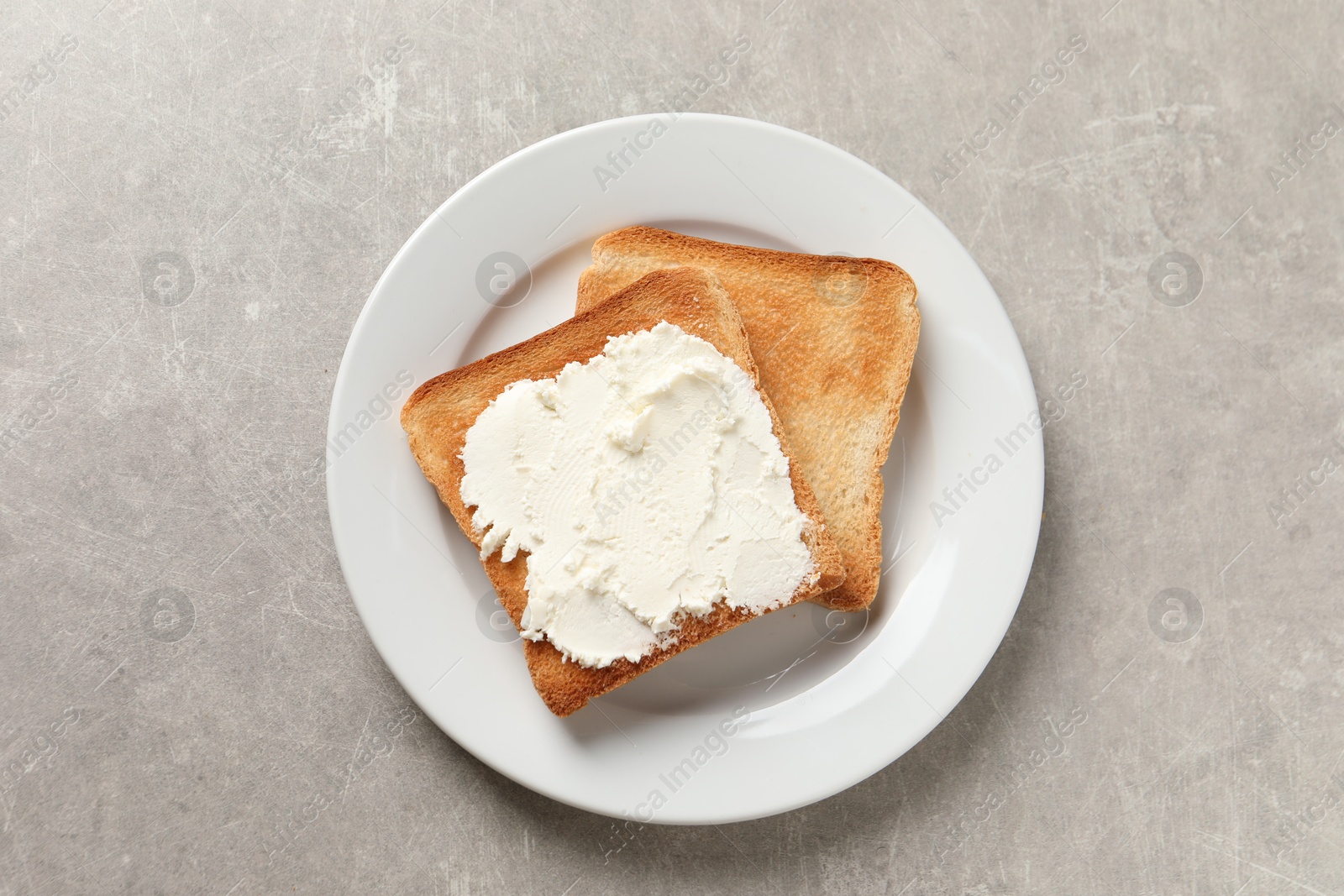 Photo of Delicious toasted bread slices with cream cheese on grey textured table, top view