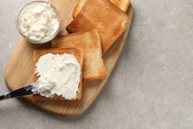 Delicious toasted bread slices with cream cheese and knife on grey textured table, top view. Space for text