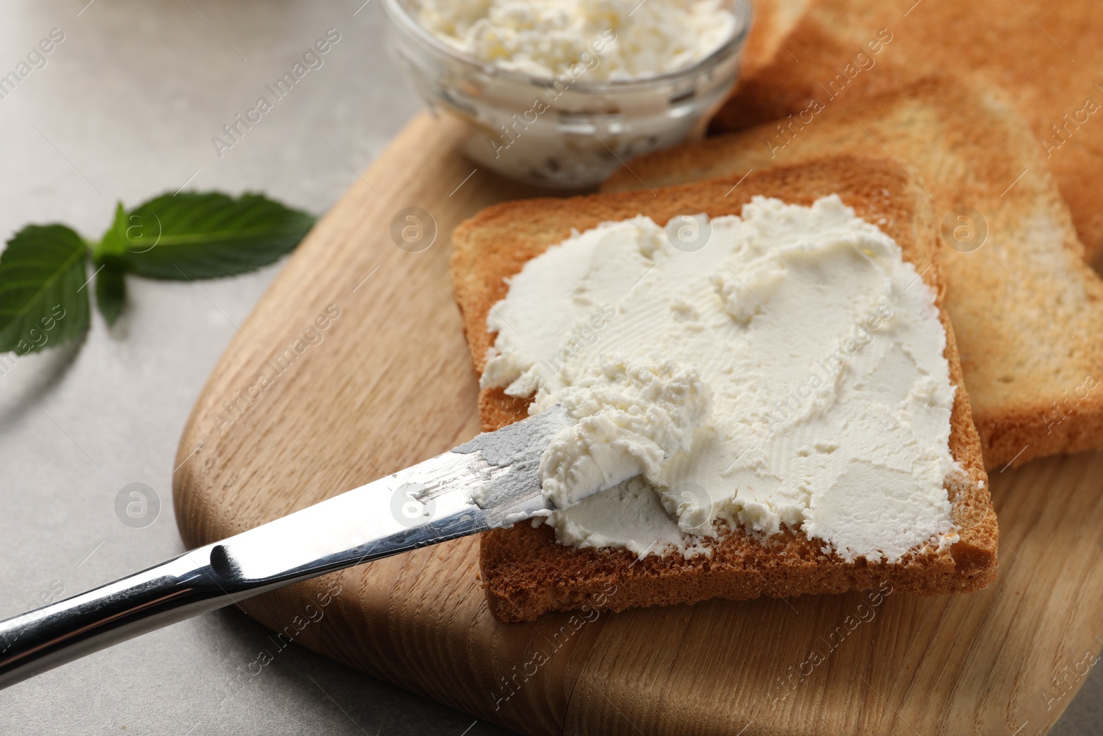 Photo of Delicious toasted bread slices with cream cheese and knife on grey table, closeup