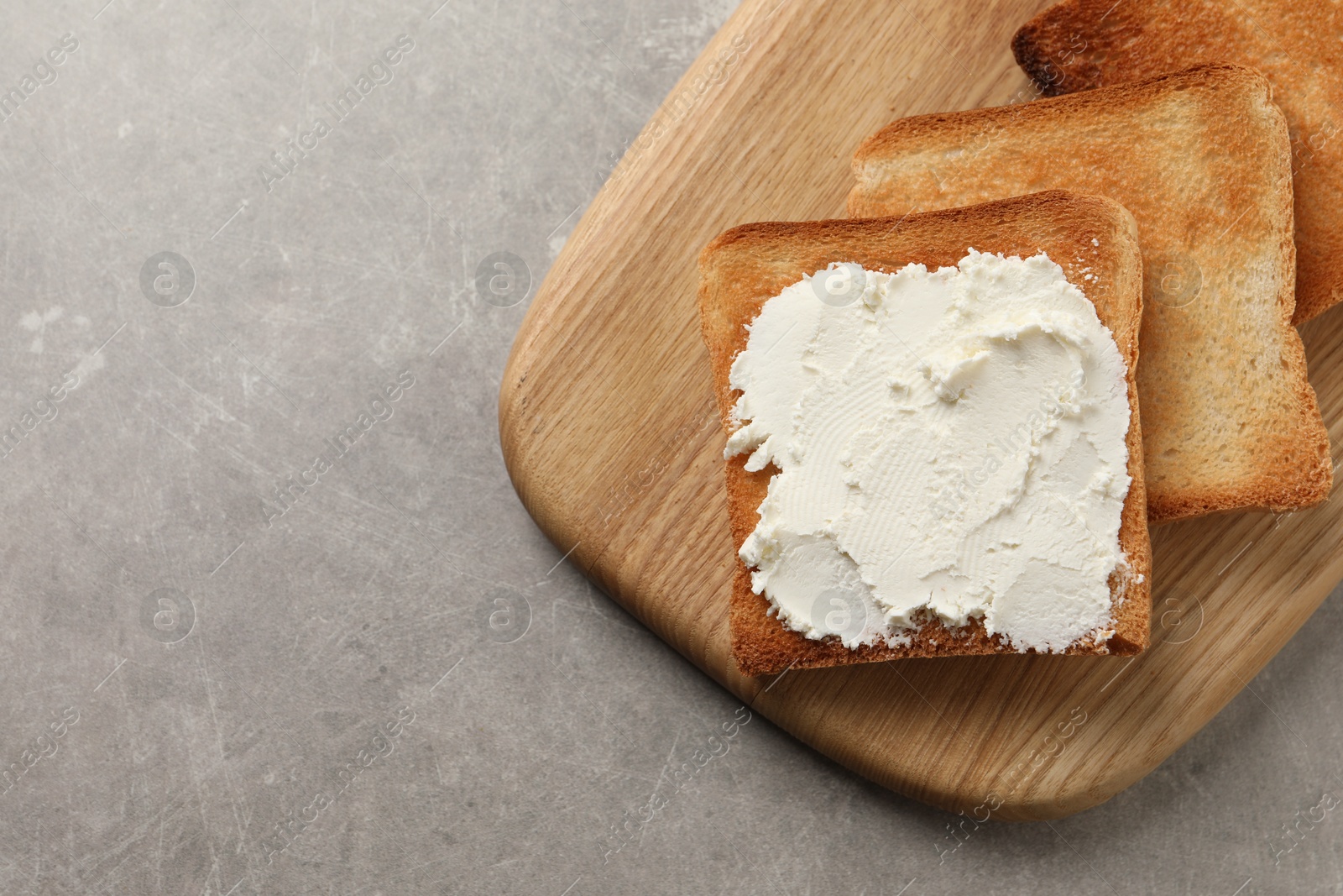 Photo of Delicious toasted bread slices with cream cheese on grey textured table, top view. Space for text