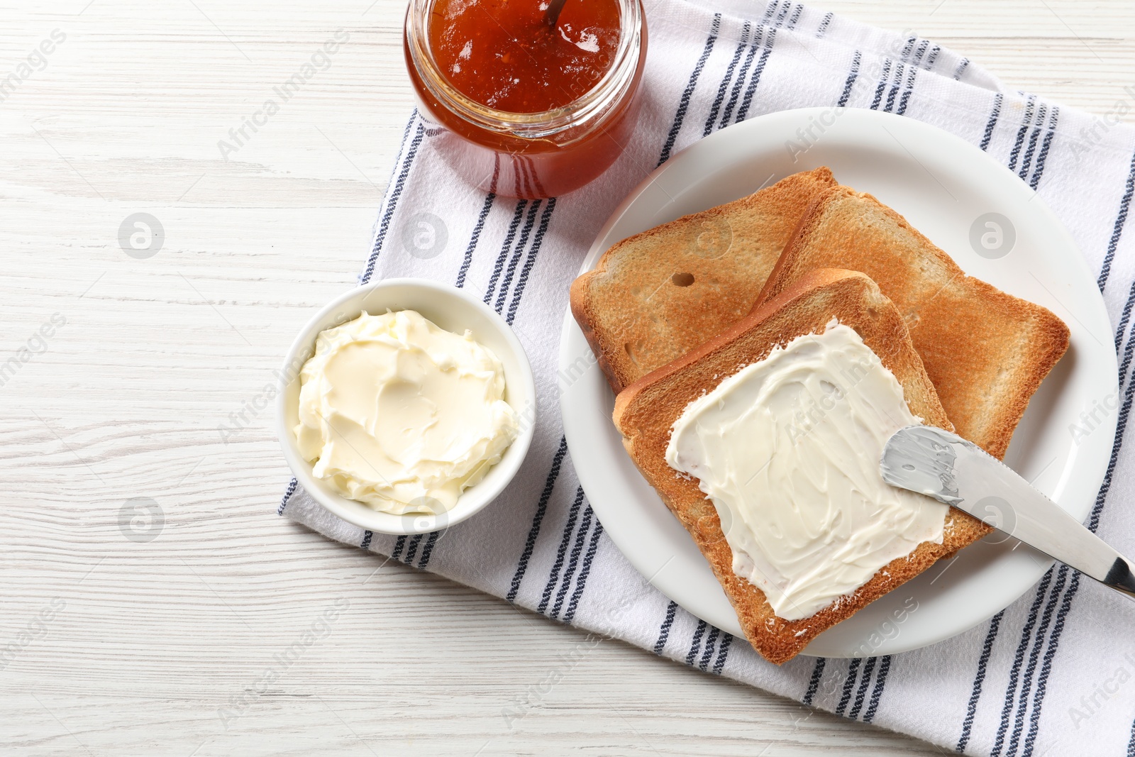 Photo of Delicious toasted bread slices with jam and knife on white wooden table, flat lay