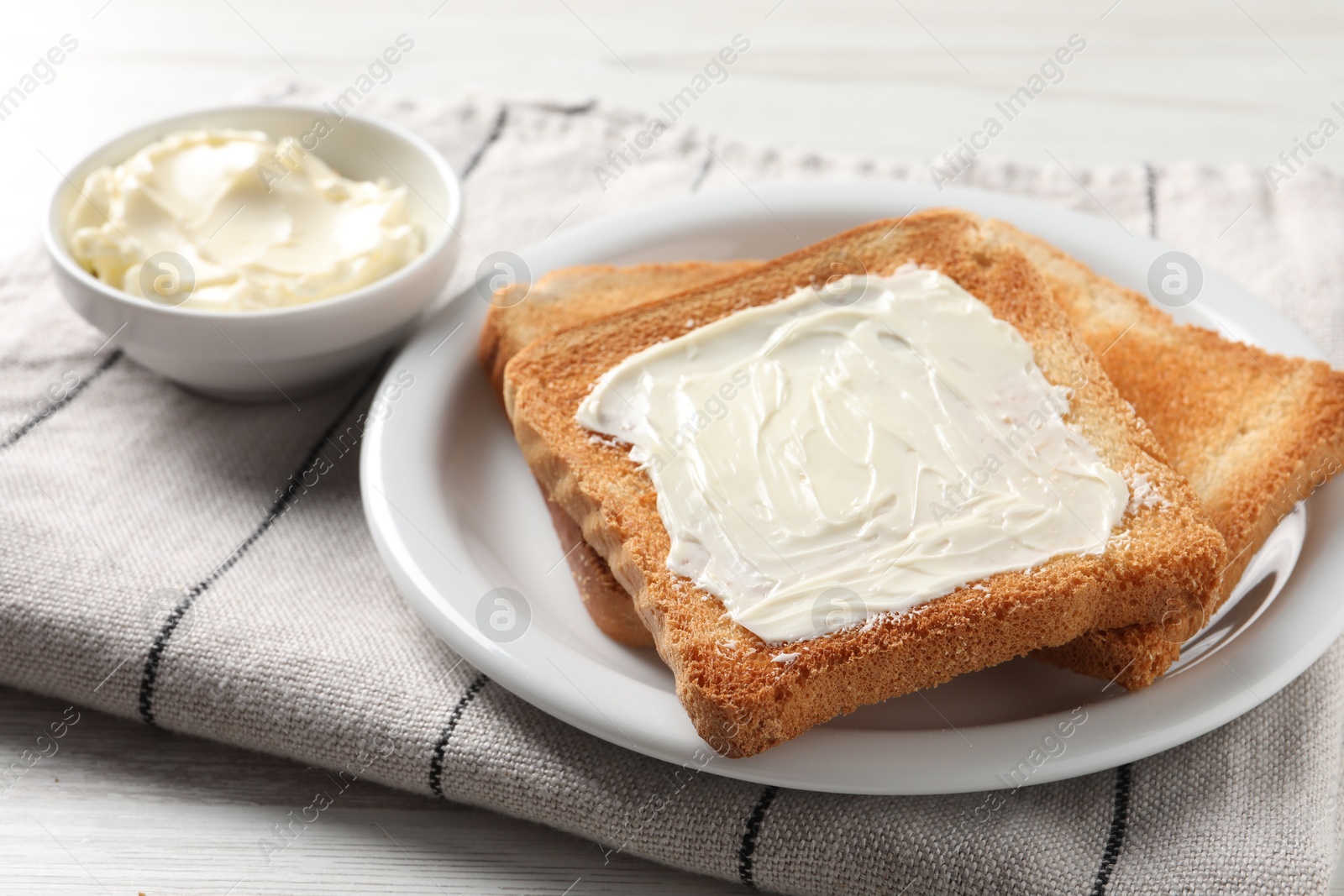 Photo of Delicious toasted bread slices with butter on white table, closeup