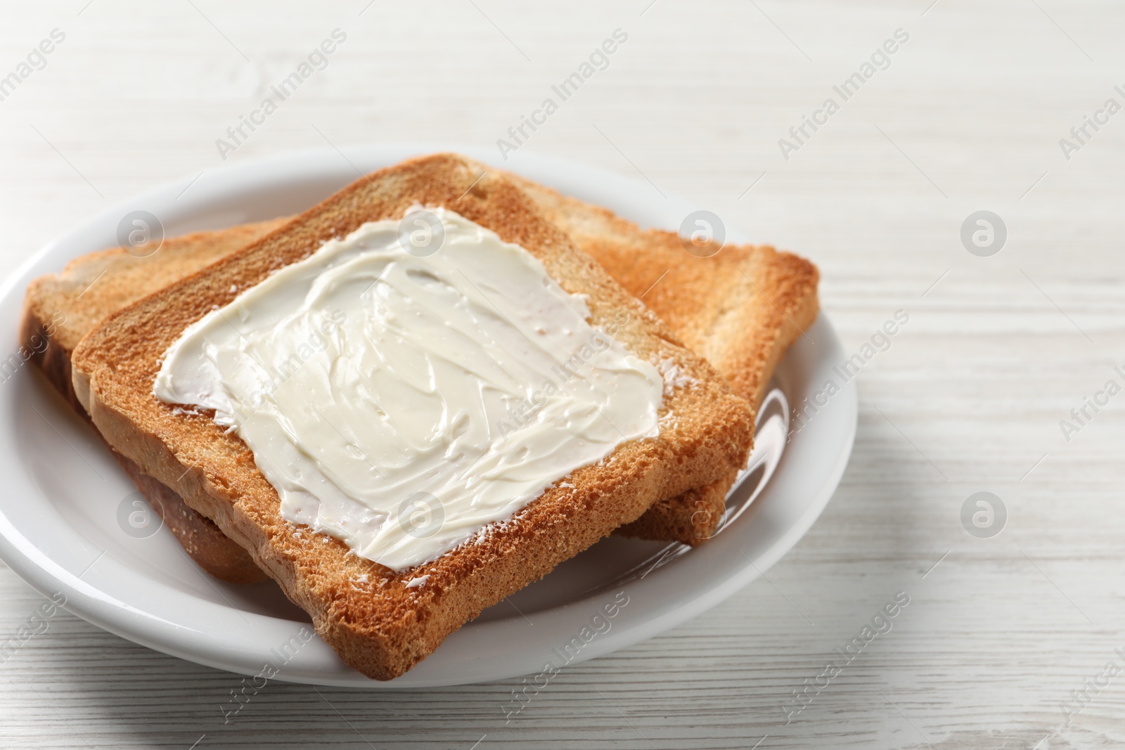 Photo of Delicious toasted bread slices with butter on white wooden table, closeup