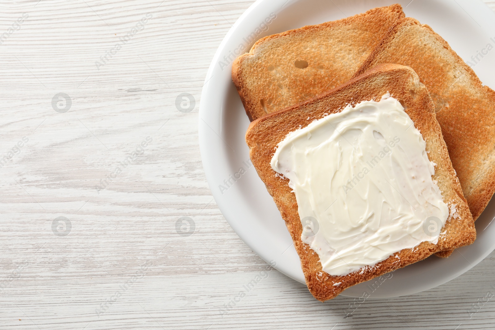 Photo of Delicious toasted bread slices with butter on white wooden table, top view. Space for text