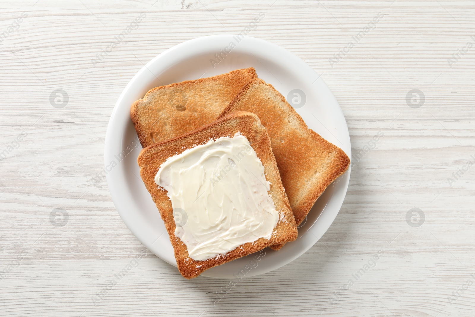 Photo of Delicious toasted bread slices with butter on white wooden table, top view