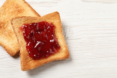 Photo of Delicious toasted bread slices with jam on white wooden table, top view. Space for text