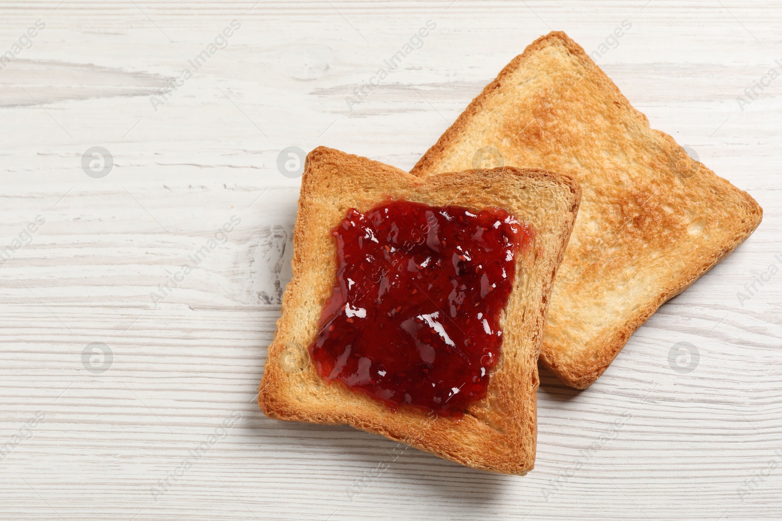 Photo of Delicious toasted bread slices with jam on white wooden table, top view