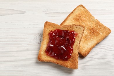 Delicious toasted bread slices with jam on white wooden table, top view