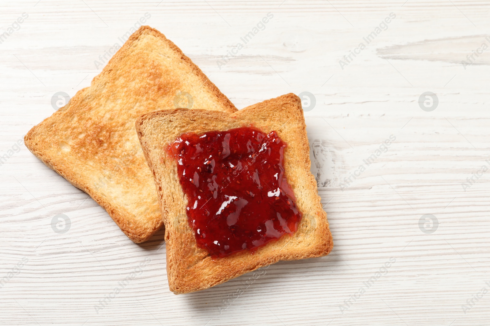 Photo of Delicious toasted bread slices with jam on white wooden table, top view