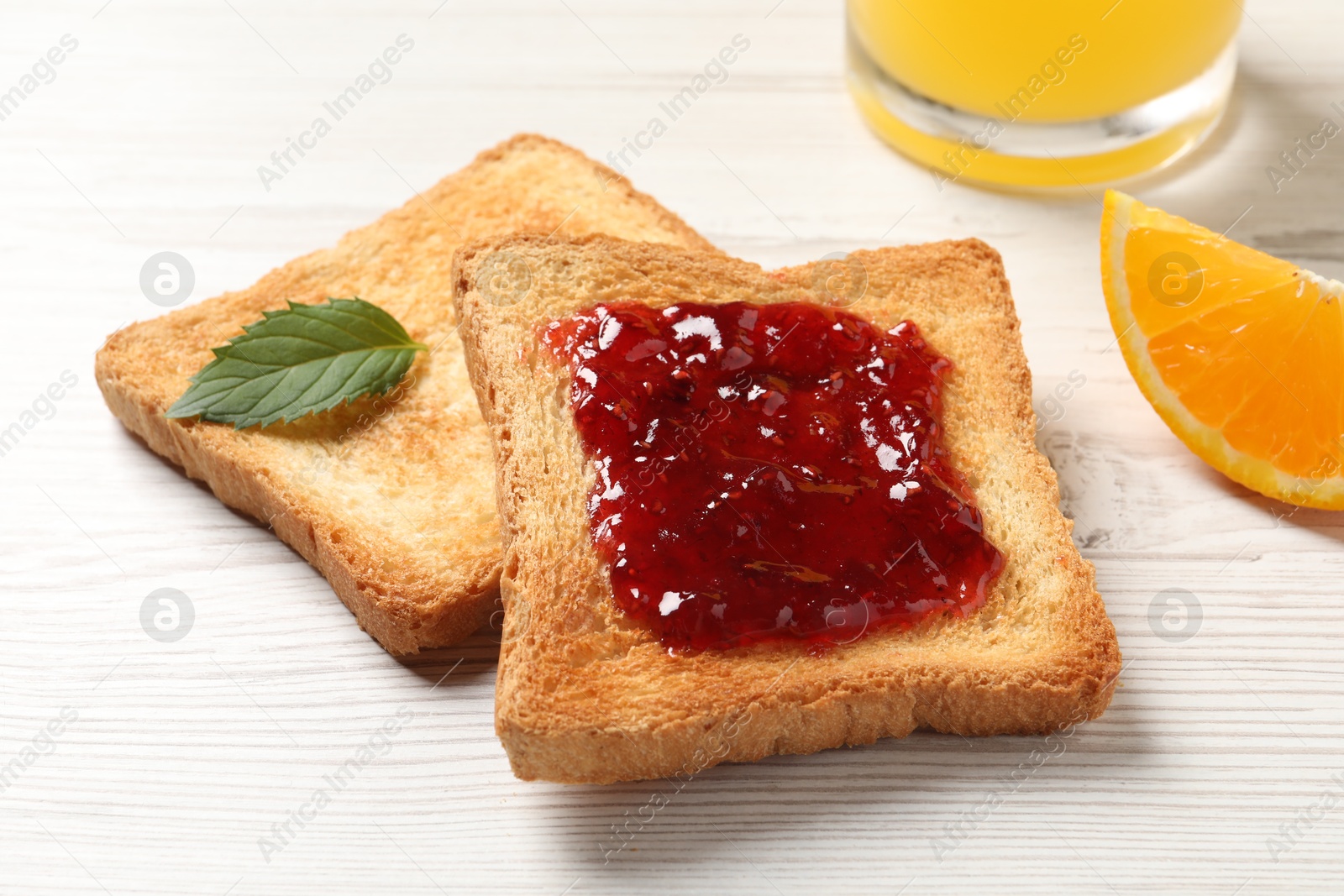 Photo of Delicious toasted bread slices with jam and mint on white wooden table