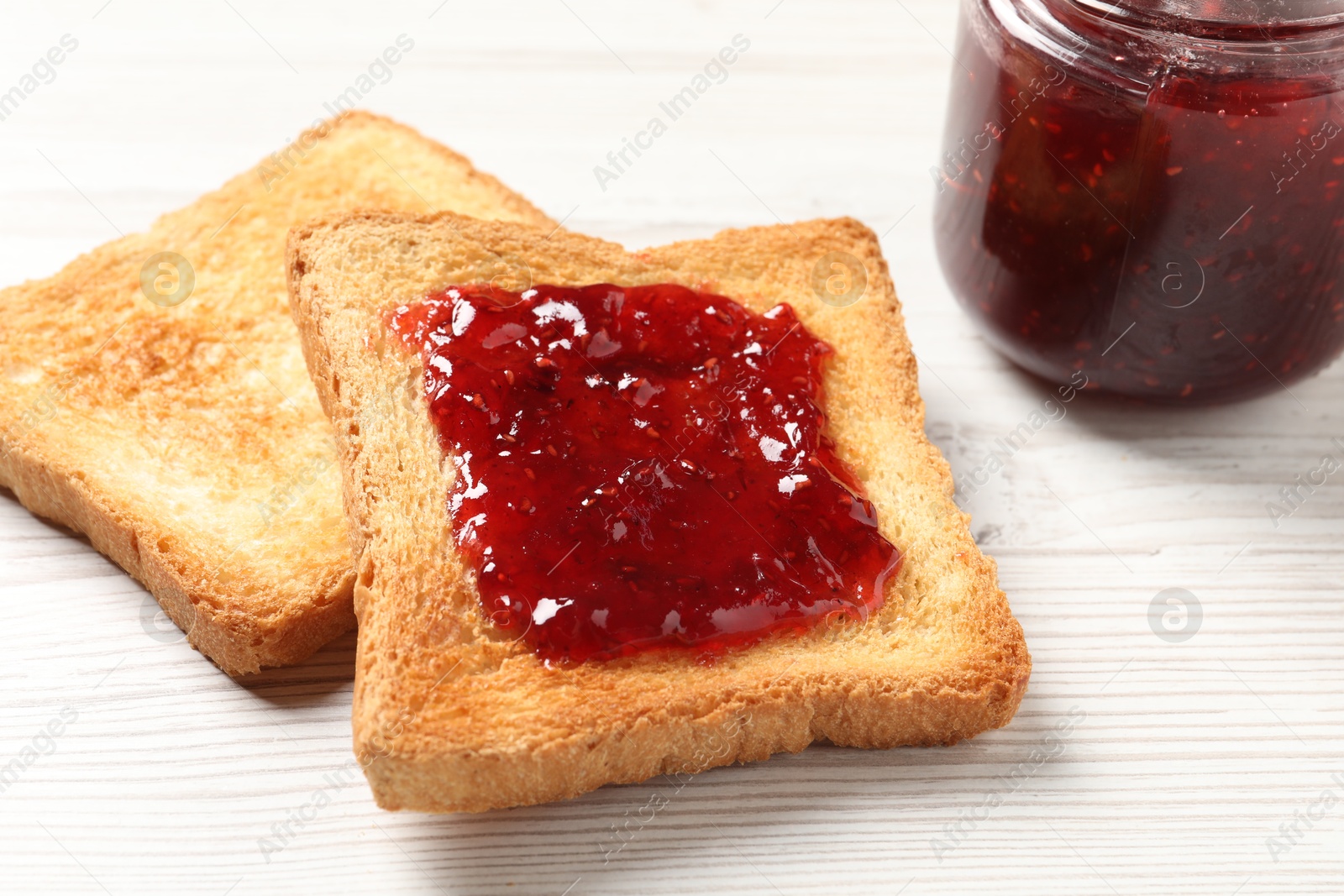 Photo of Delicious toasted bread slices with jam on white wooden table, closeup