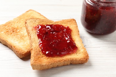 Delicious toasted bread slices with jam on white wooden table, closeup