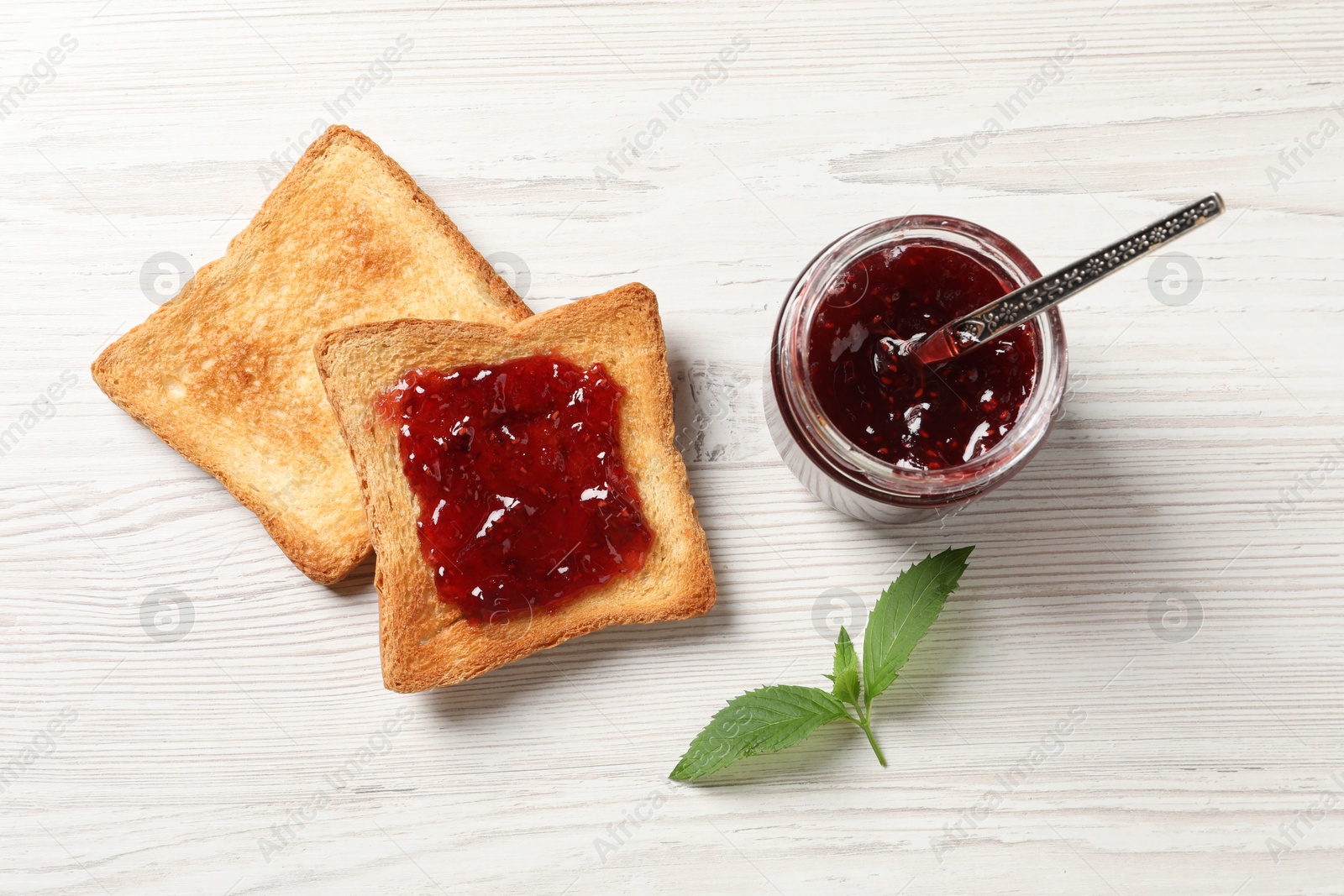 Photo of Delicious toasted bread slices with jam and mint on white wooden table, flat lay