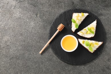 Delicious bruschettas with ricotta cheese, pear, mint and honey on grey textured table, top view. Space for text