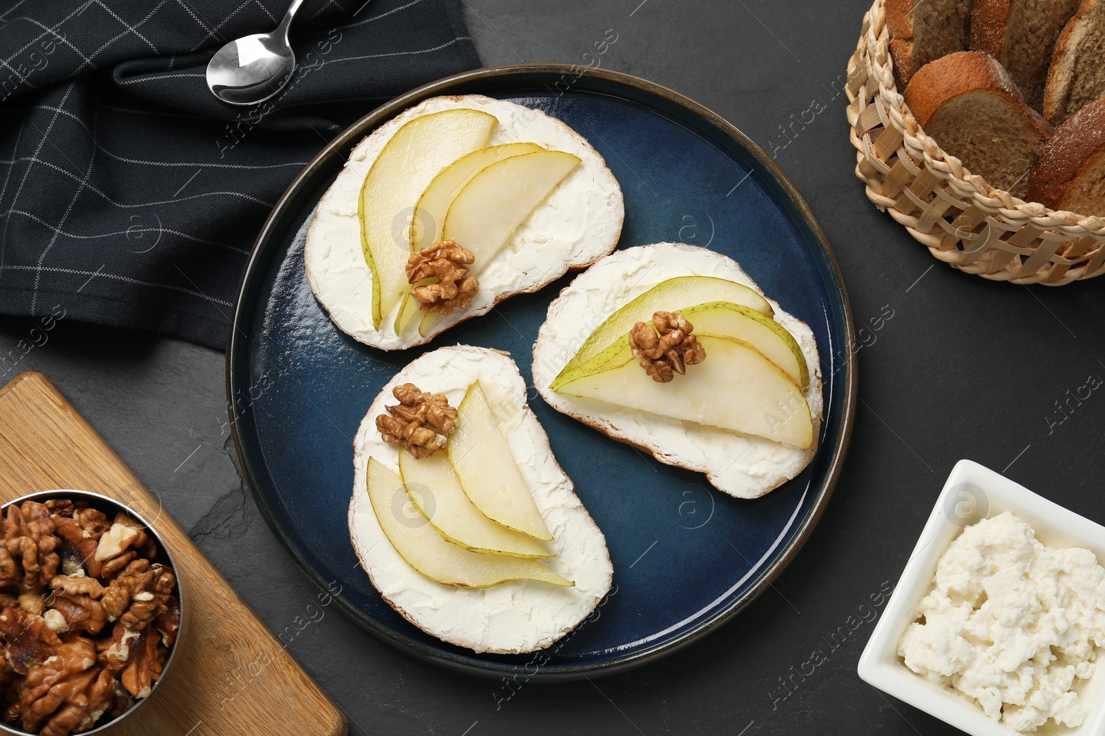 Photo of Delicious bruschettas with ricotta cheese, pears and walnuts on dark textured table, flat lay