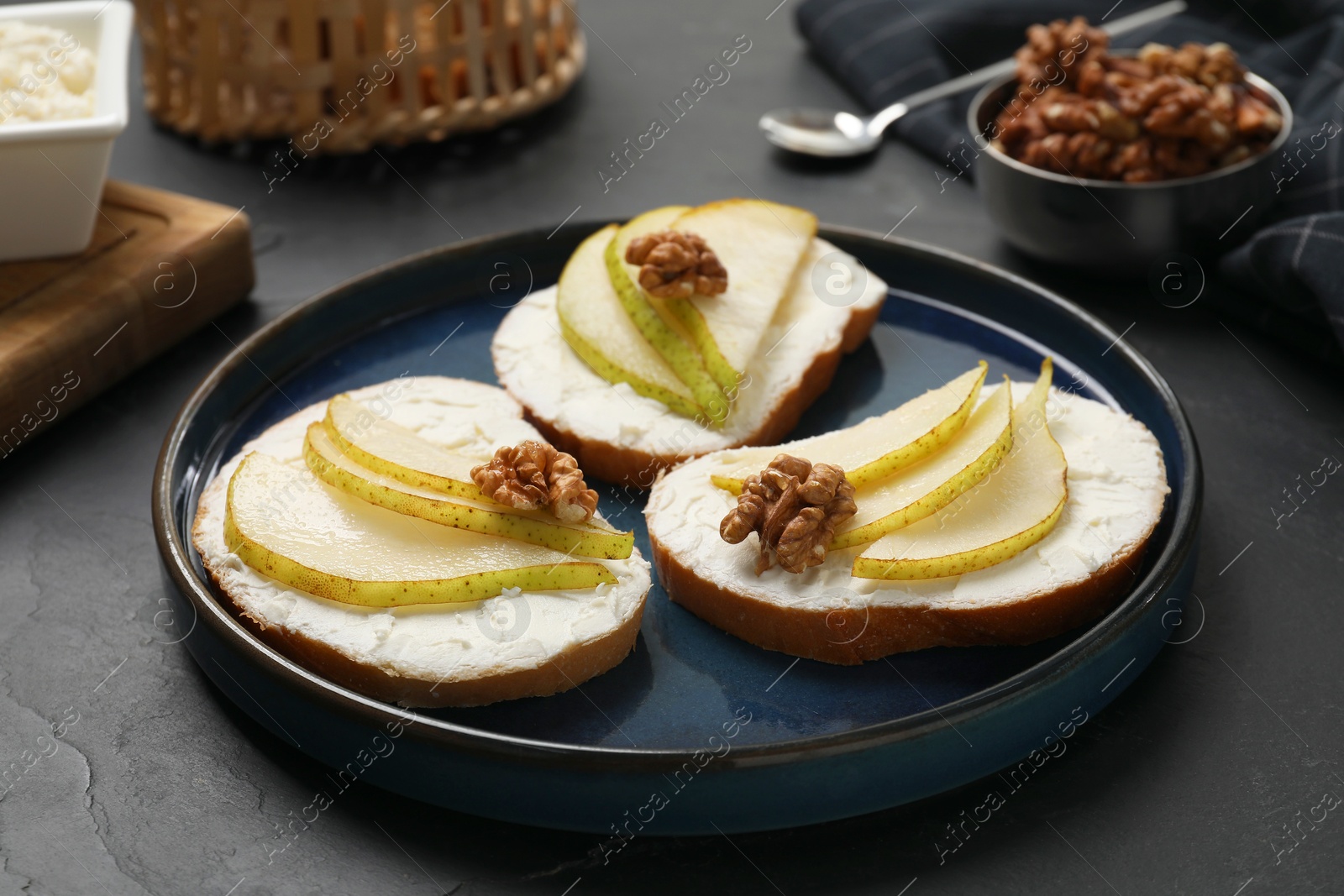 Photo of Delicious bruschettas with ricotta cheese, pears and walnuts on dark textured table, closeup