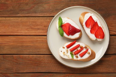 Delicious bruschettas with ricotta cheese, walnuts, mint and strawberries on wooden table, top view. Space for text