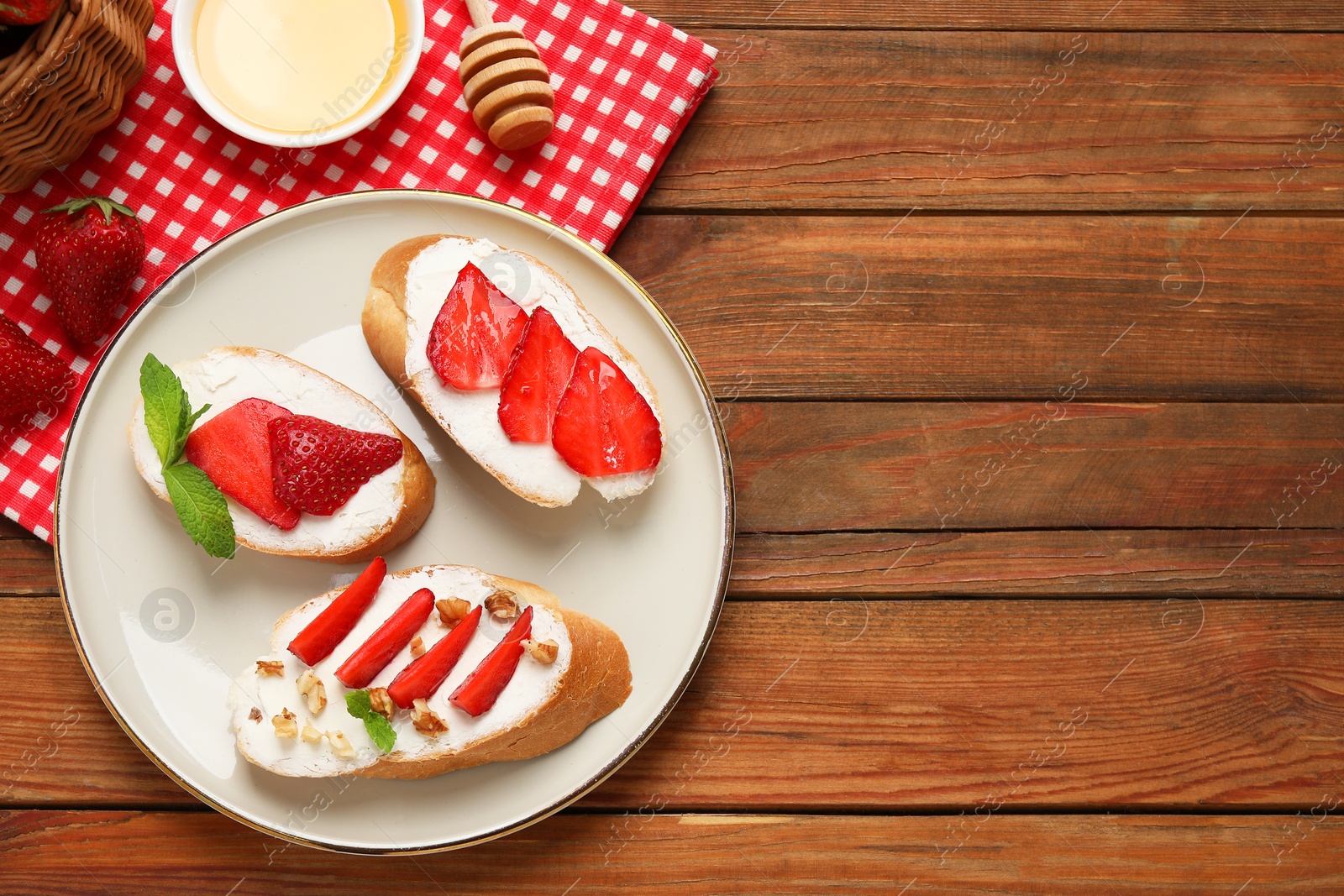 Photo of Delicious bruschettas with ricotta cheese, walnuts, mint, strawberries and honey on wooden table, flat lay. Space for text