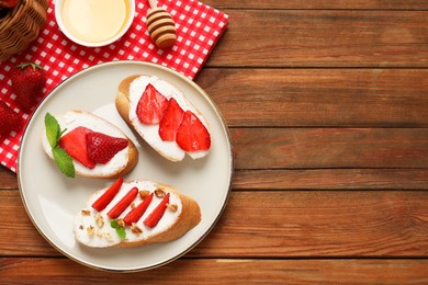 Photo of Delicious bruschettas with ricotta cheese, walnuts, mint, strawberries and honey on wooden table, flat lay. Space for text